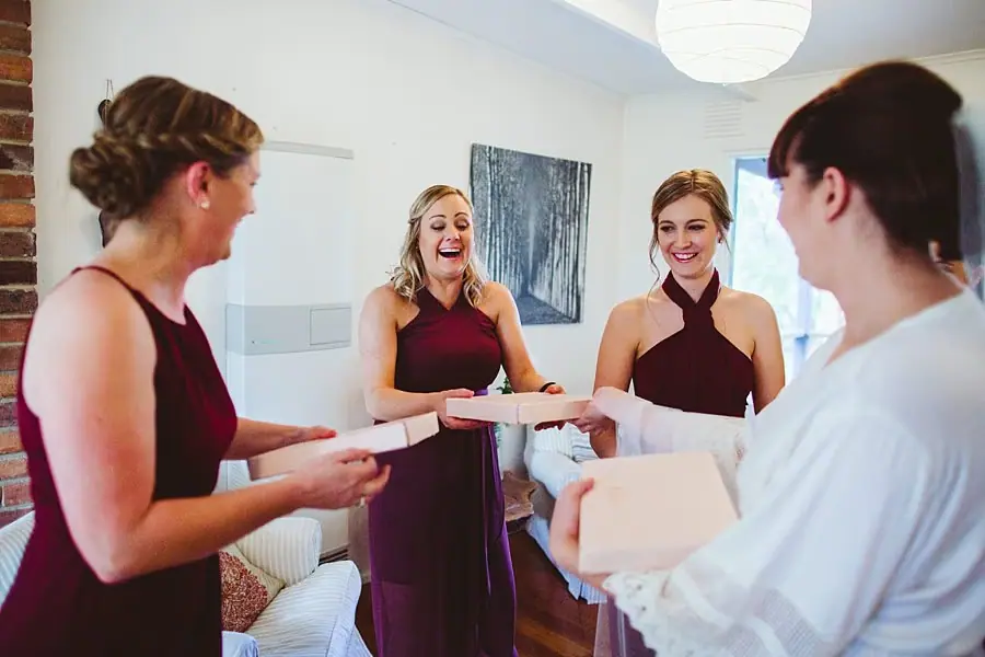 Bride handing cards to smiling women in burgundy dresses.