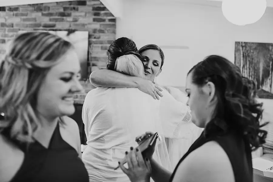 Black-and-white photograph of women embracing and looking at a phone indoors.