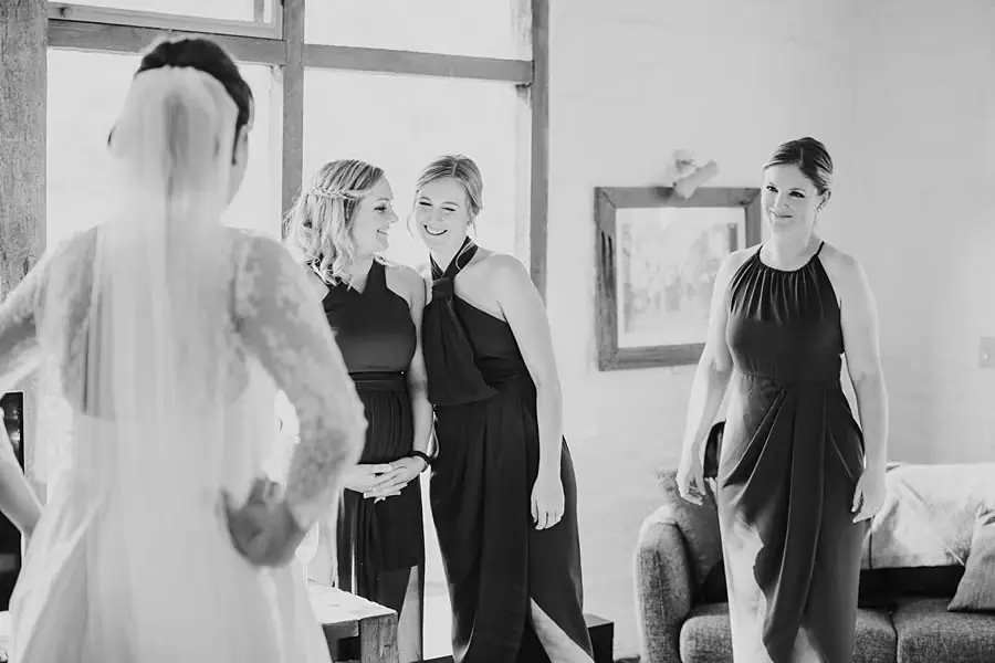 Black-and-white photograph of the bride showing her dress to three smiling women.