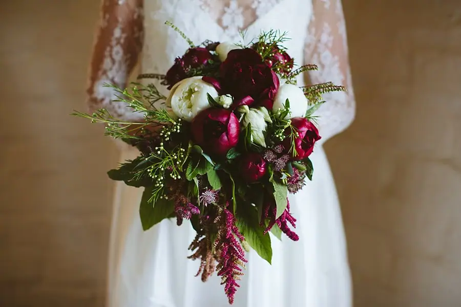 Close-up of the bride holding a burgundy-and-white bouquet with trailing greenery.