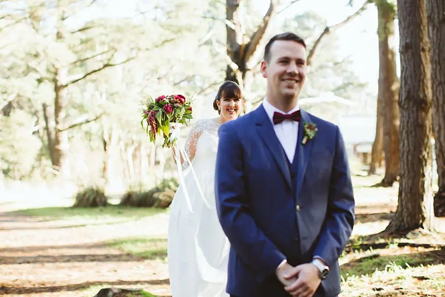 Groom waiting on a wooded path as the bride approaches holding her bouquet.