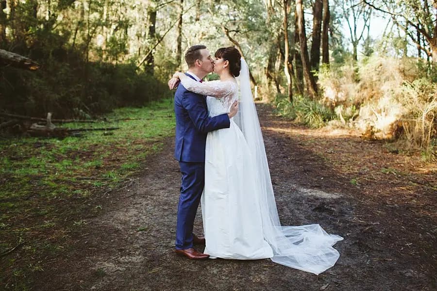Bride and groom embracing on a sunlit woodland path.