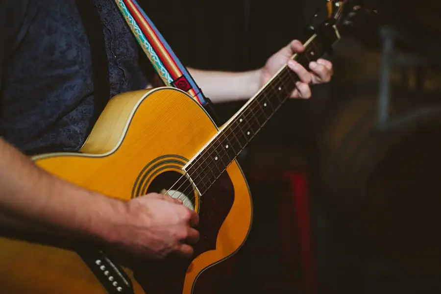 Close-up of a musician playing an acoustic guitar with a striped shoulder strap.