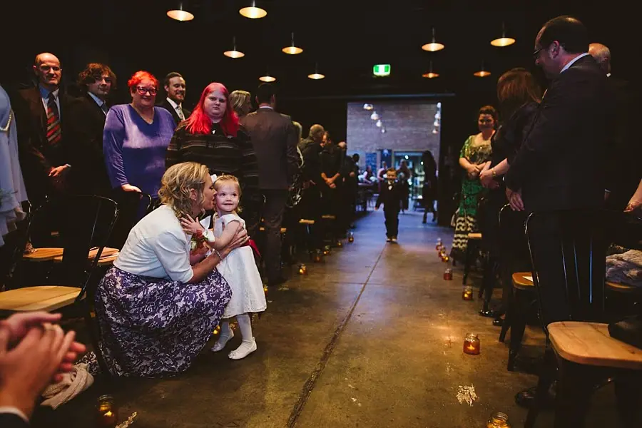 Guests standing beside a candle-lined ceremony aisle as a woman embraces a young child.