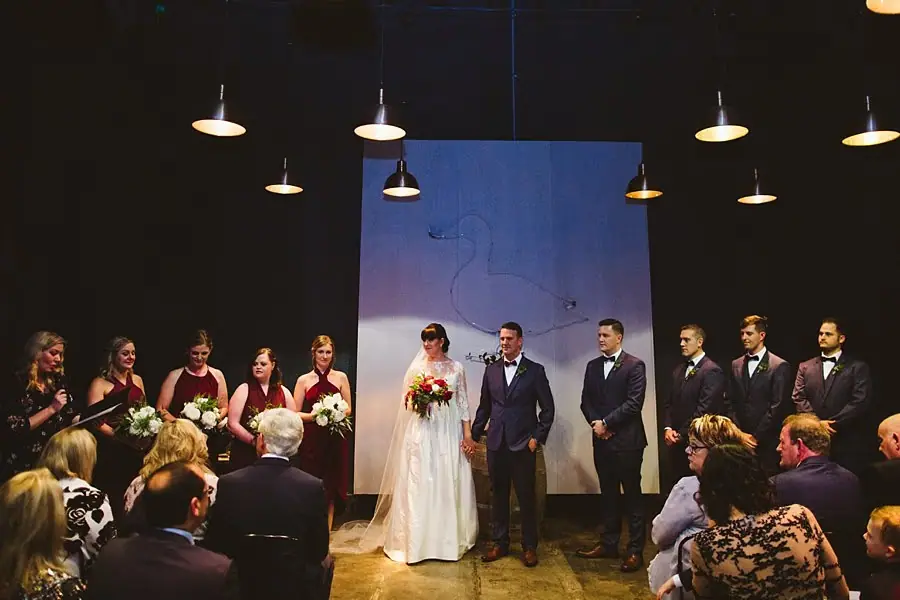 Bride and groom standing with the wedding party during an indoor ceremony.