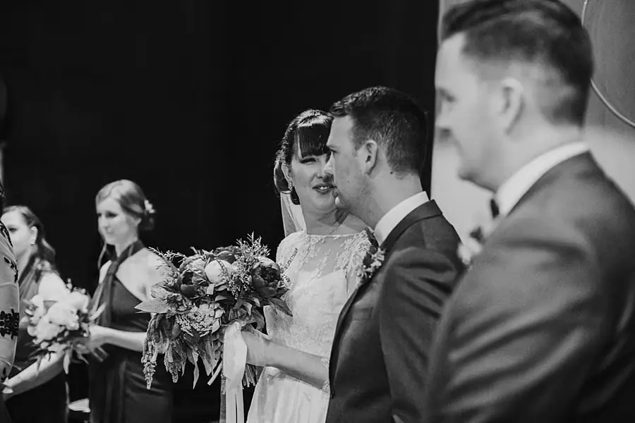Black-and-white photograph of the couple standing with the wedding party during the ceremony.