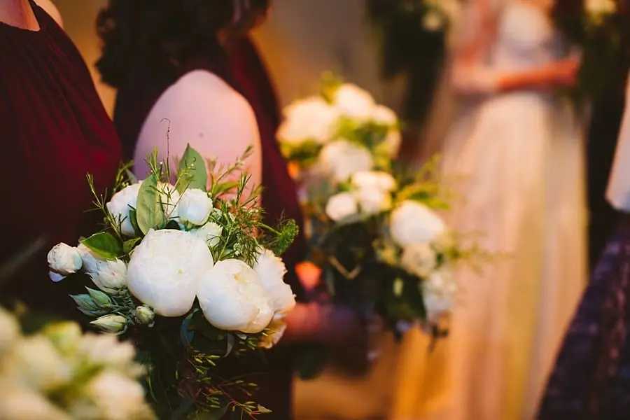 Close-up of white bouquets held by women in burgundy dresses during the ceremony.