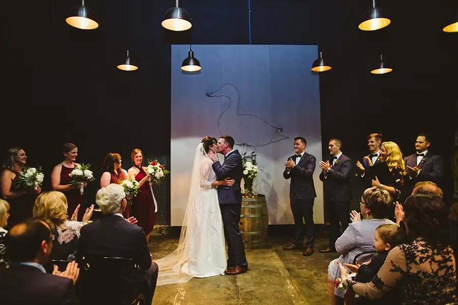Bride and groom kissing while the wedding party and guests applaud.
