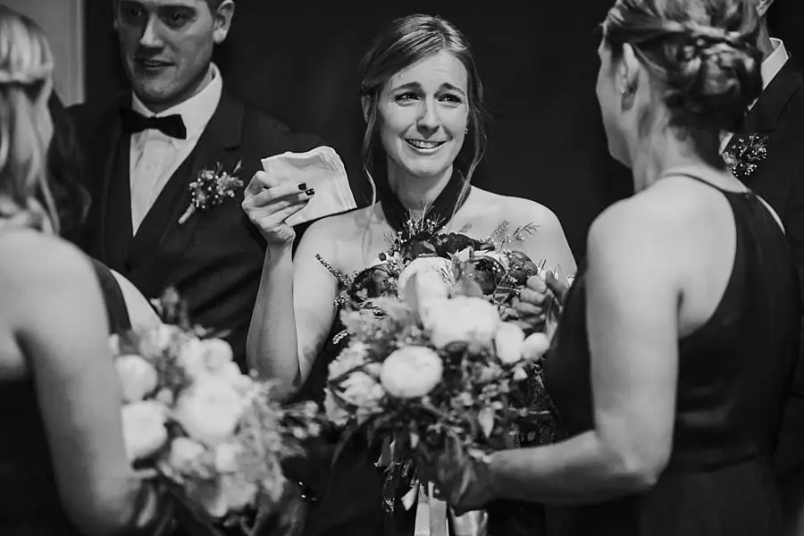 Black-and-white photograph of wedding-party members greeting each other with bouquets in hand.