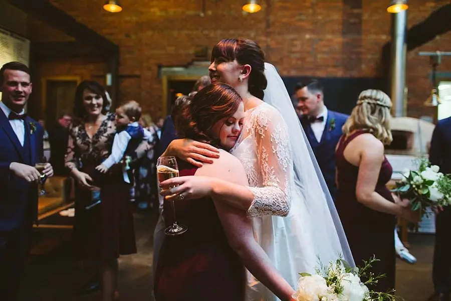 Bride embracing a woman in burgundy among wedding guests.