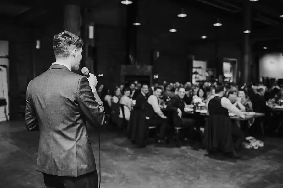 Black-and-white photograph of a man giving a speech to seated reception guests.
