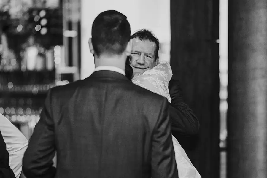 Black-and-white photograph of the groom greeting a man carrying a young child.