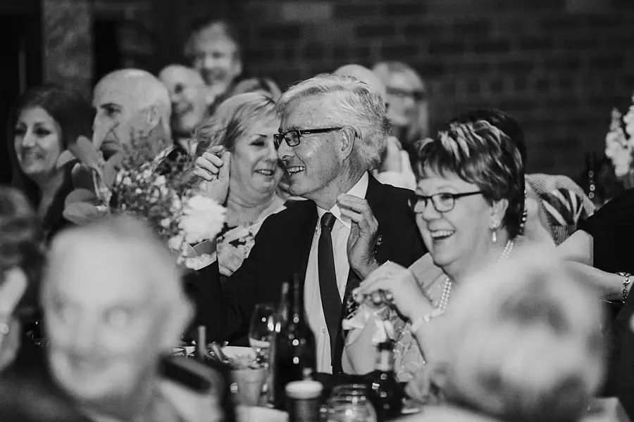 Black-and-white photograph of smiling guests seated at a reception table.