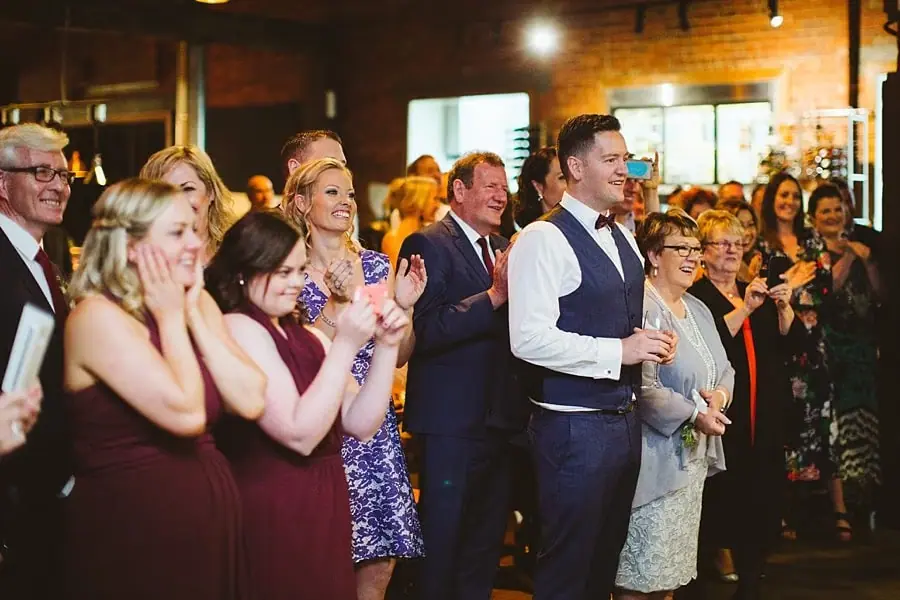 Reception guests smiling and applauding as they watch the couple dance.