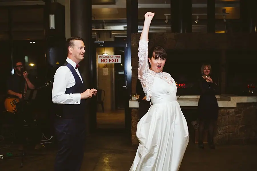 Bride raising one arm in the air while dancing beside the groom.