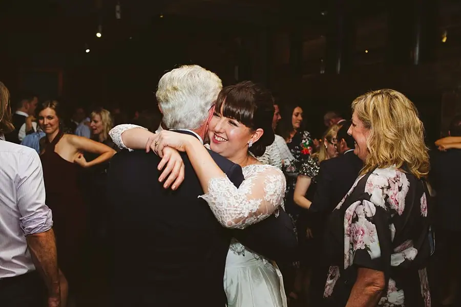 Bride smiling as she embraces an older suited guest on the dance floor.