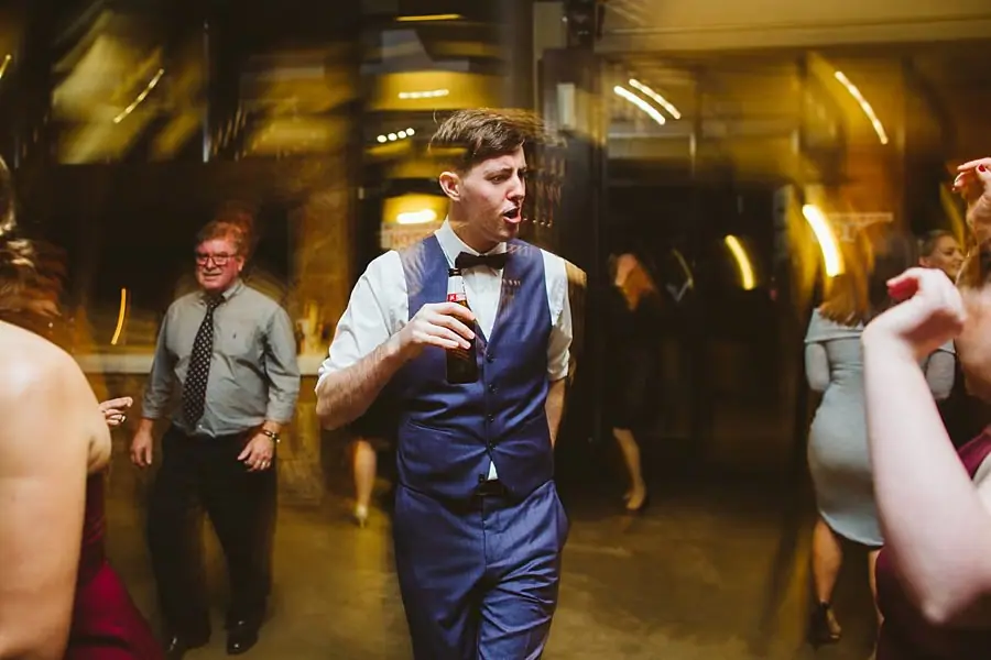 Man in a blue waistcoat dancing among reception guests.