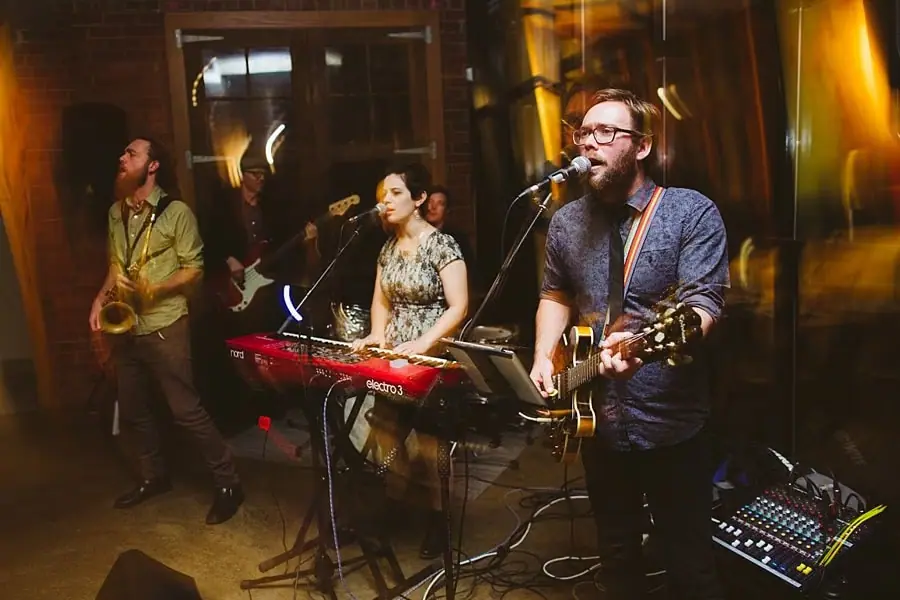 Guitarist singing beside a keyboard player and saxophonist performing at the reception.