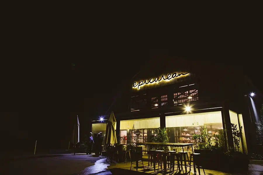 Illuminated restaurant entrance and outdoor tables at night.
