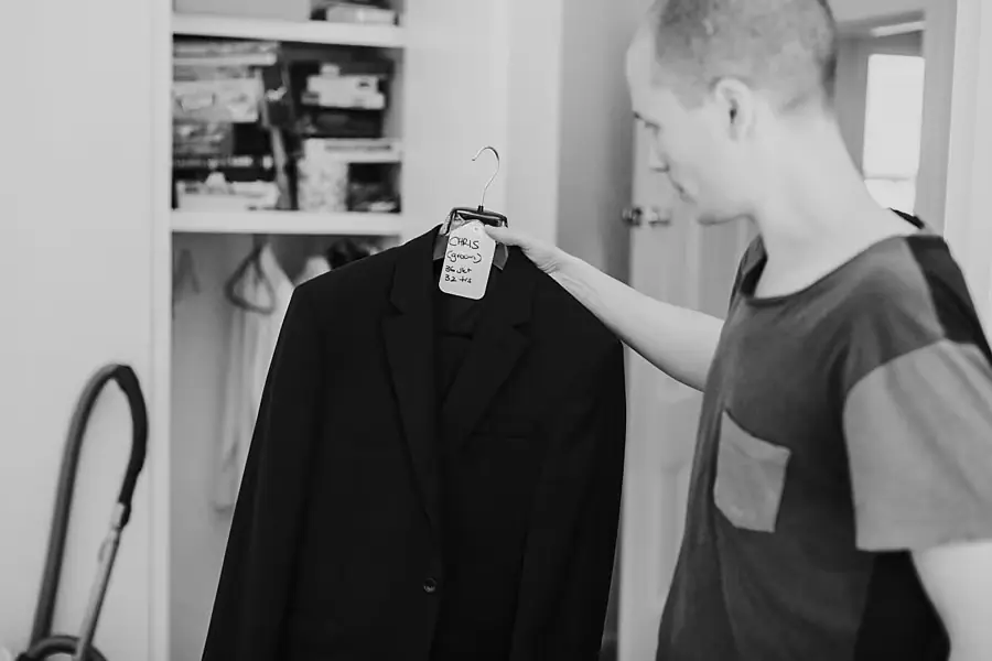 Black-and-white photograph of a man holding up a black suit jacket while getting ready.