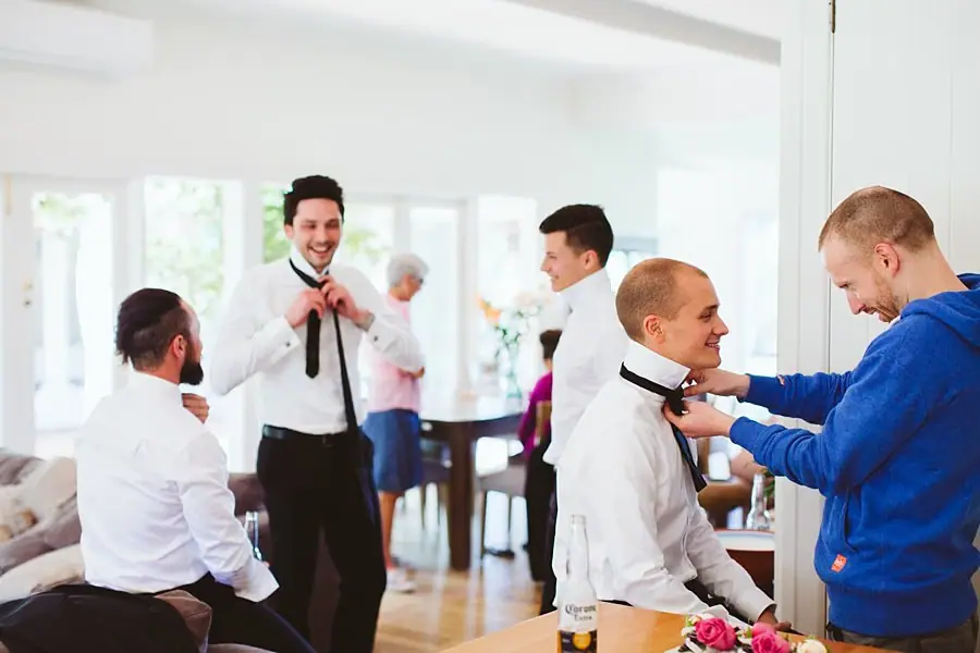 Men adjusting ties and helping each other dress in white shirts before the wedding.