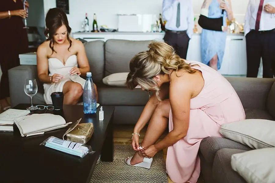 Woman in a pink dress bending down to fasten a shoe while another woman sits nearby.