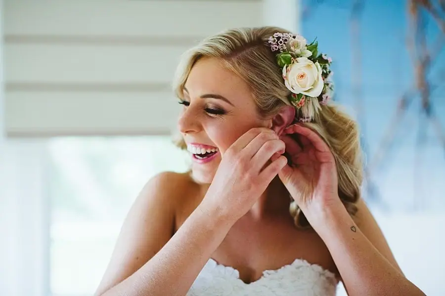Bride smiling while adjusting an earring, with flowers tucked into her hair.
