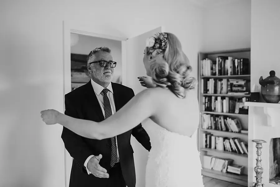 Black-and-white photograph of a bride embracing a man wearing glasses and a dark suit.