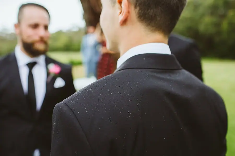 Close view of a man’s dark wedding suit with other men standing behind him.