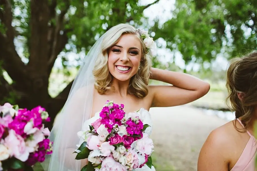 Bride smiling while touching the back of her hair beside her bridesmaids.