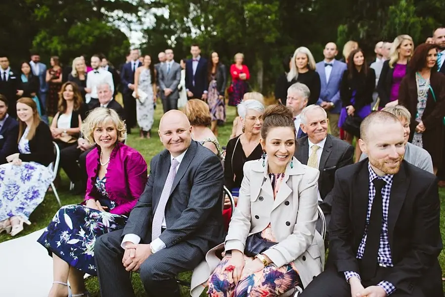 Wedding guests seated in rows on the lawn, smiling toward the ceremony.