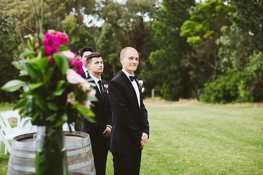 Two suited men waiting beside a floral arrangement on a wooden barrel.