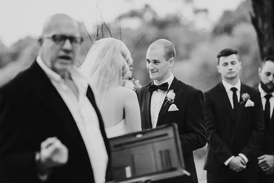 Black-and-white photograph of the bride, groom and celebrant during their outdoor ceremony.