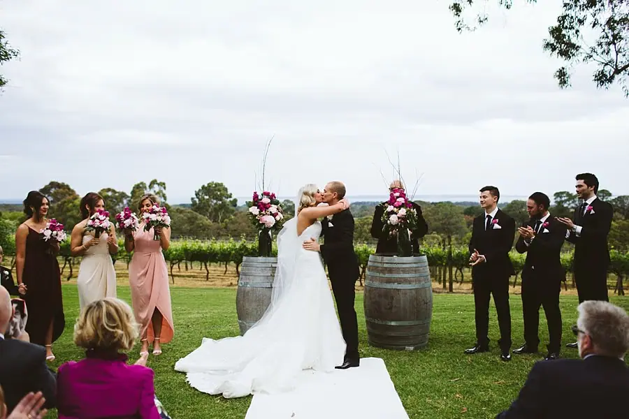 Bride and groom kissing during their ceremony as the wedding party looks on.