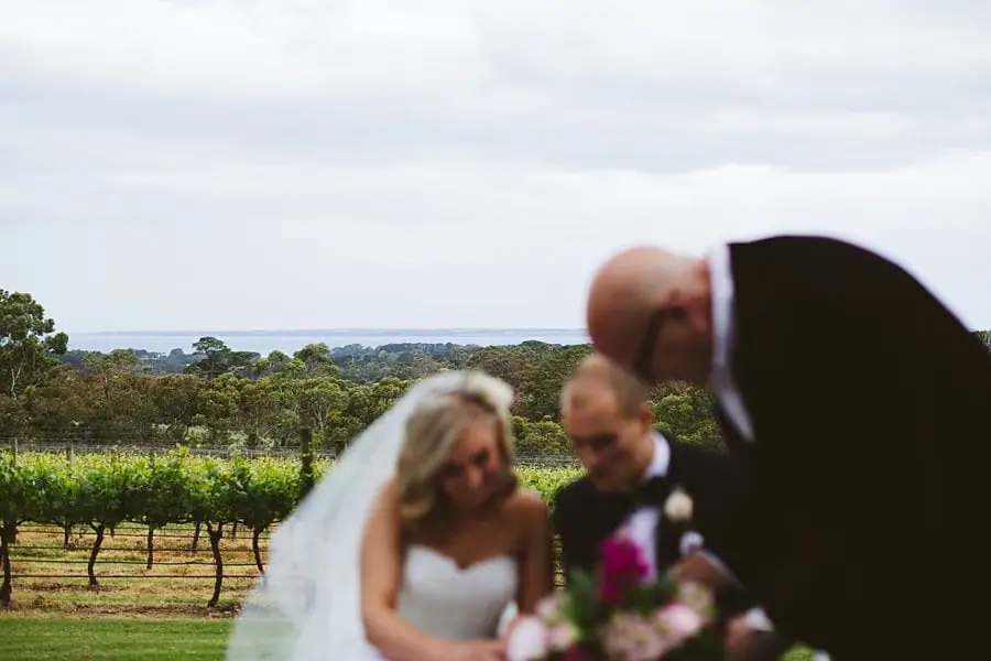 Bride and groom bending over a table with the celebrant beside them and vines behind.