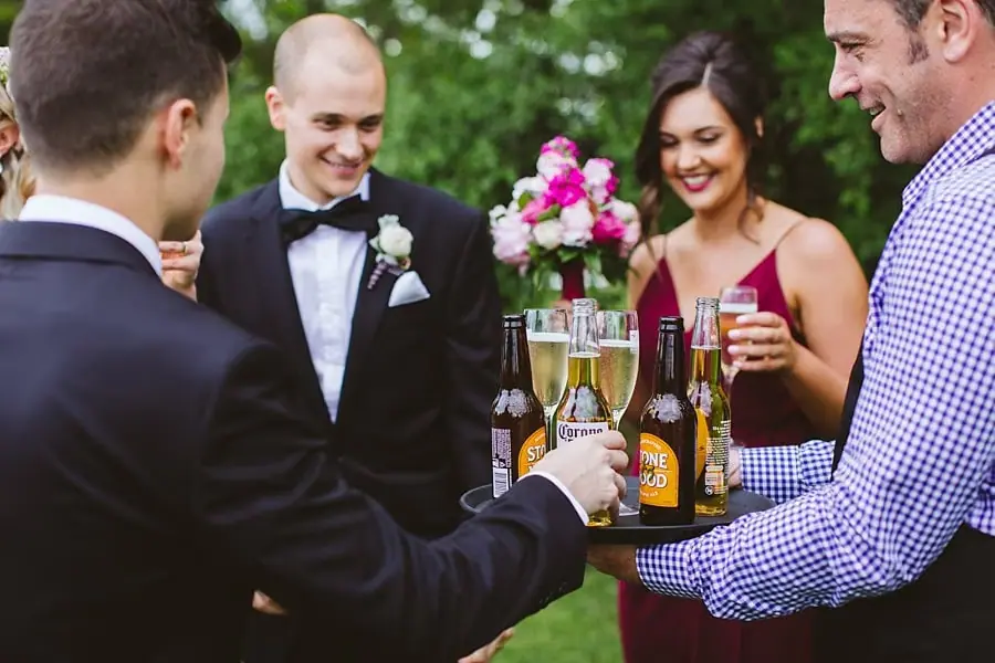 Newlyweds and friends laughing together while holding drinks outdoors.