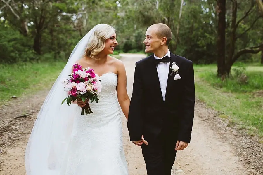 Bride and groom looking at each other while walking together along a woodland path.