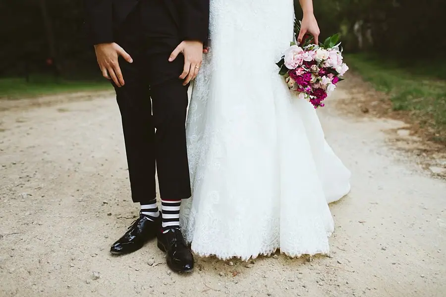 Lower-body detail of the groom’s striped socks and the bride’s lace dress with her bouquet.