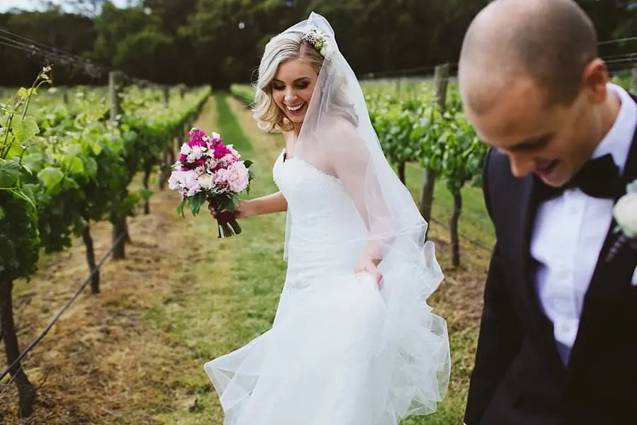 Bride holding her bouquet and walking beside the groom while both look down and smile.