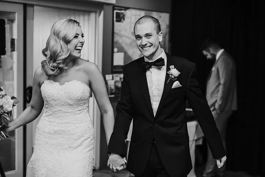 Black-and-white photograph of newlyweds entering the reception hand in hand.