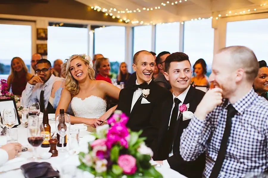 Newlyweds and friends sitting together at the reception table with drinks and pink flowers.