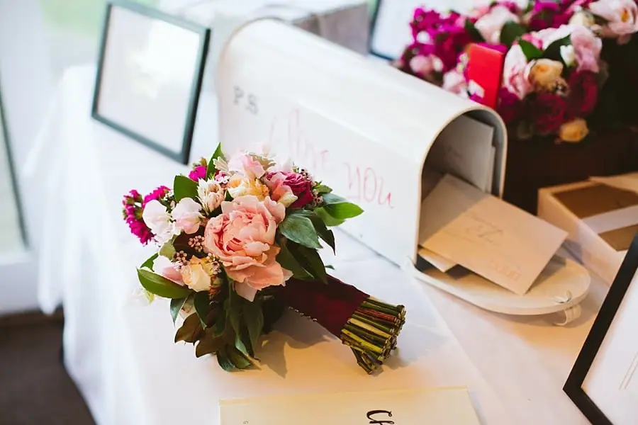 Bridal bouquet resting beside an open card box on a white reception table.