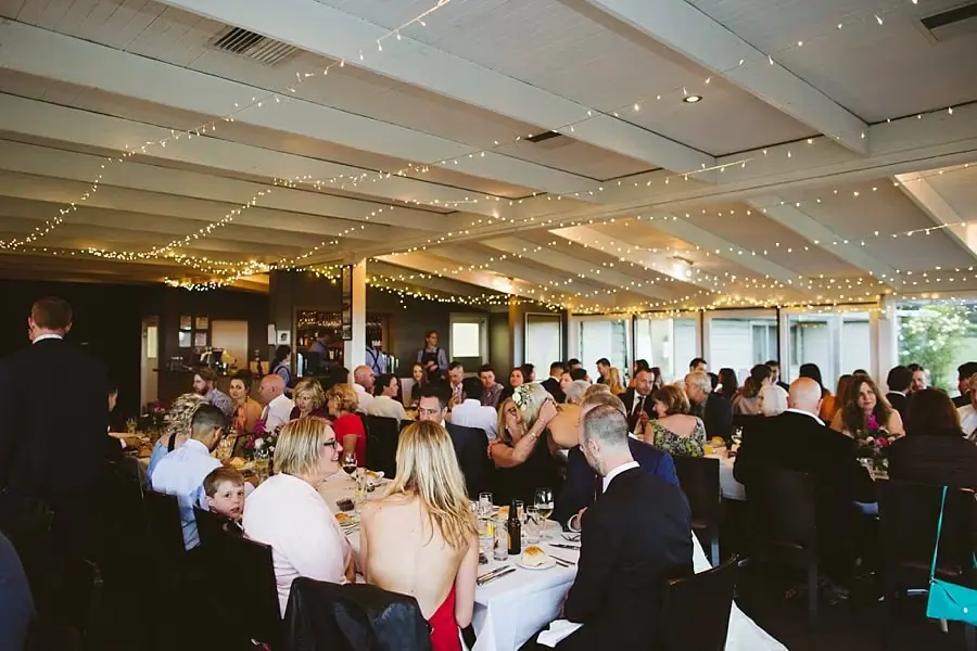 Wide view of reception guests dining beneath strings of warm ceiling lights.