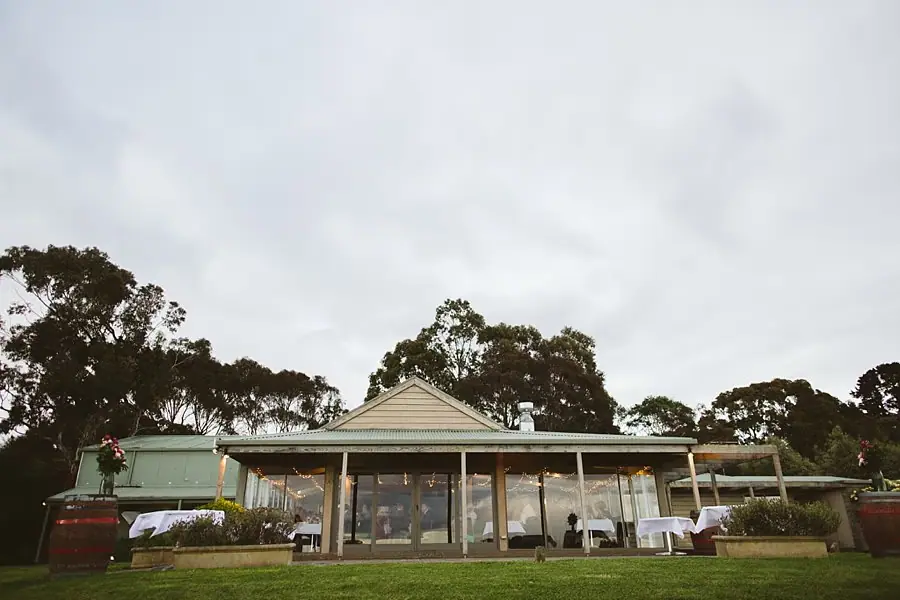Exterior view of the reception building with tables visible through large windows beneath a grey sky.