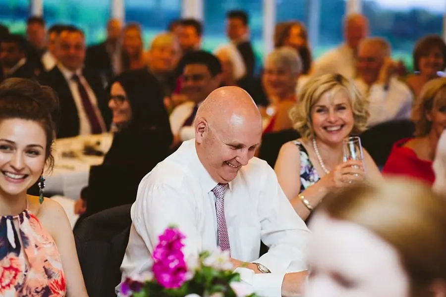 Bride and guests smiling and laughing during reception speeches.
