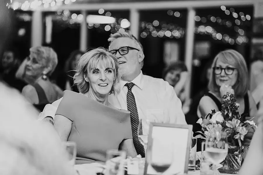 Black-and-white photograph of a woman seated at a reception table with a man leaning close behind her.