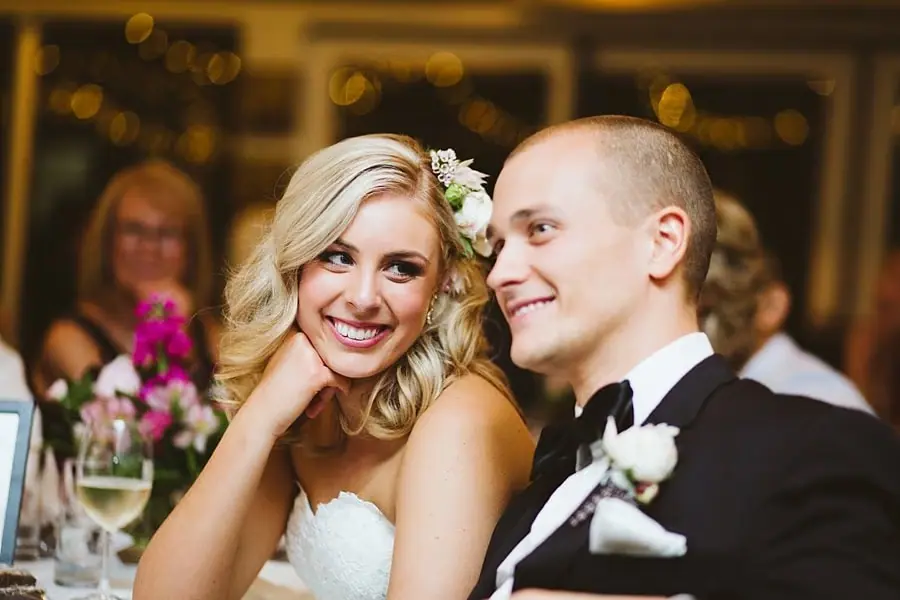 Close portrait of the bride and groom smiling together at their reception table.