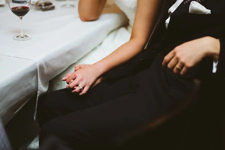 Close-up of the newlyweds holding hands beside the reception table.