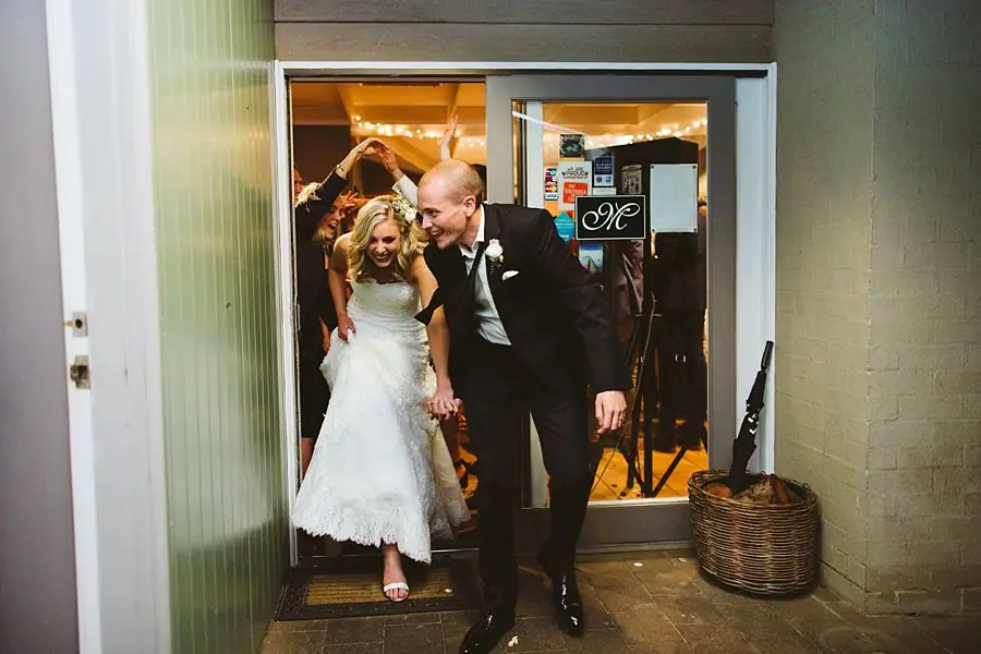 Bride and groom walking out of the reception doorway together with their arms around each other.