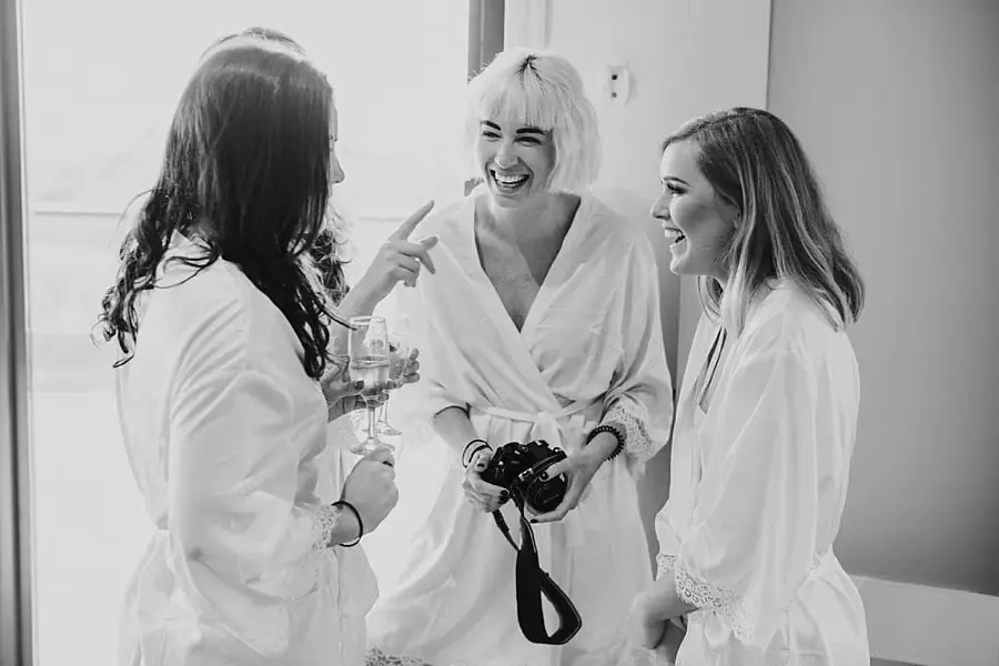 Black-and-white photograph of women laughing together in pale robes.